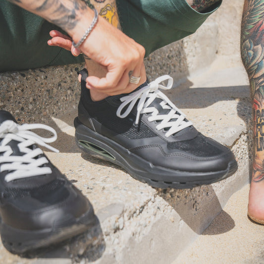Person wearing black sneakers with white laces on a concrete surface