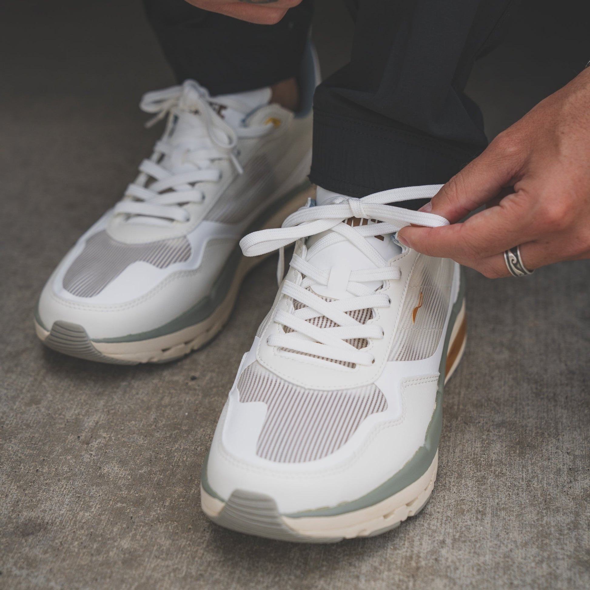 Person tying shoelaces on white sneakers with a neutral background