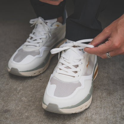 Person tying shoelaces on white sneakers with a neutral background