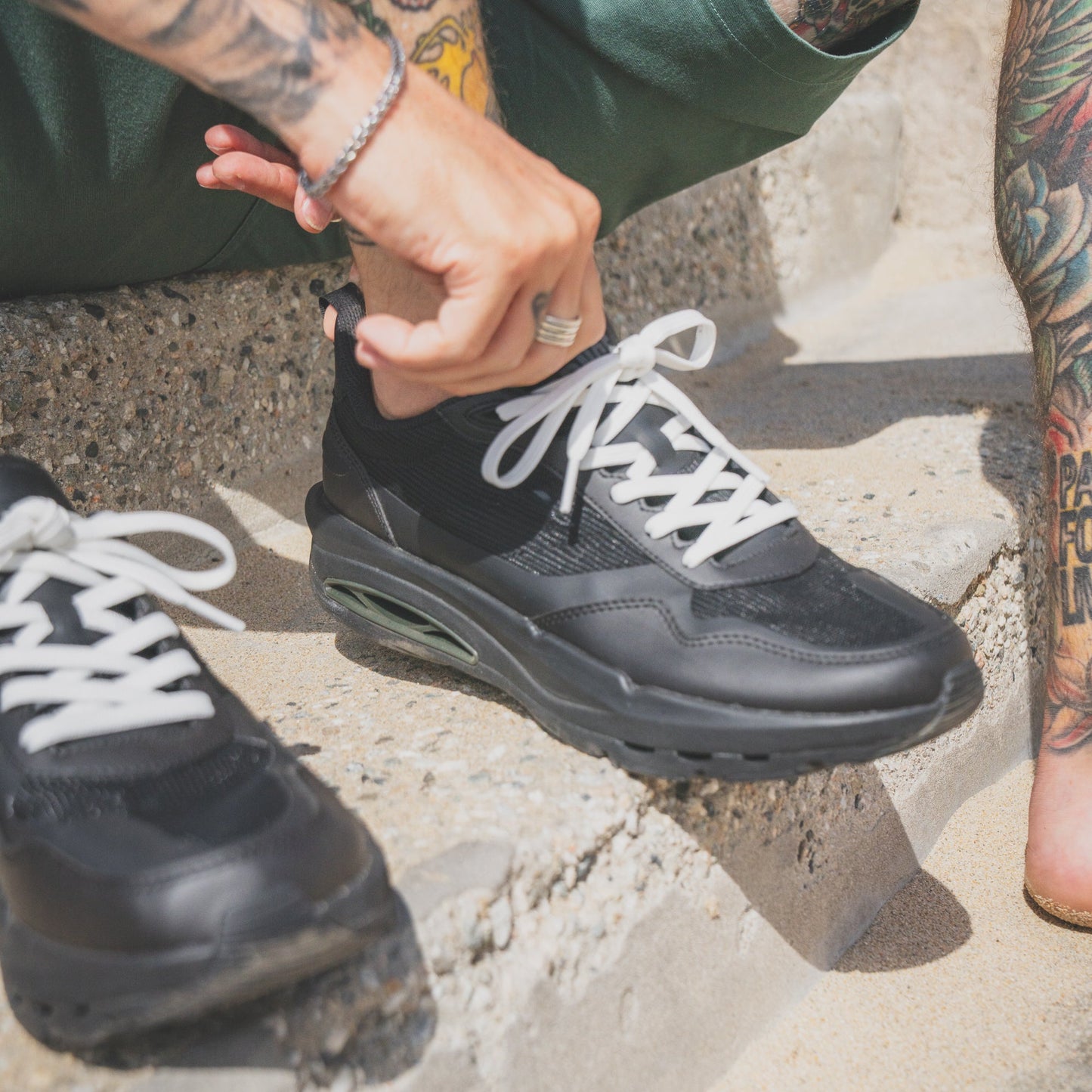 Person wearing black sneakers with white laces on a concrete surface