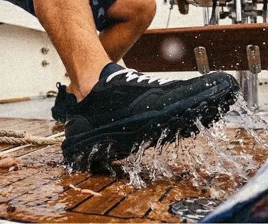 Person testing a black sneaker on a boat deck with water splashing.