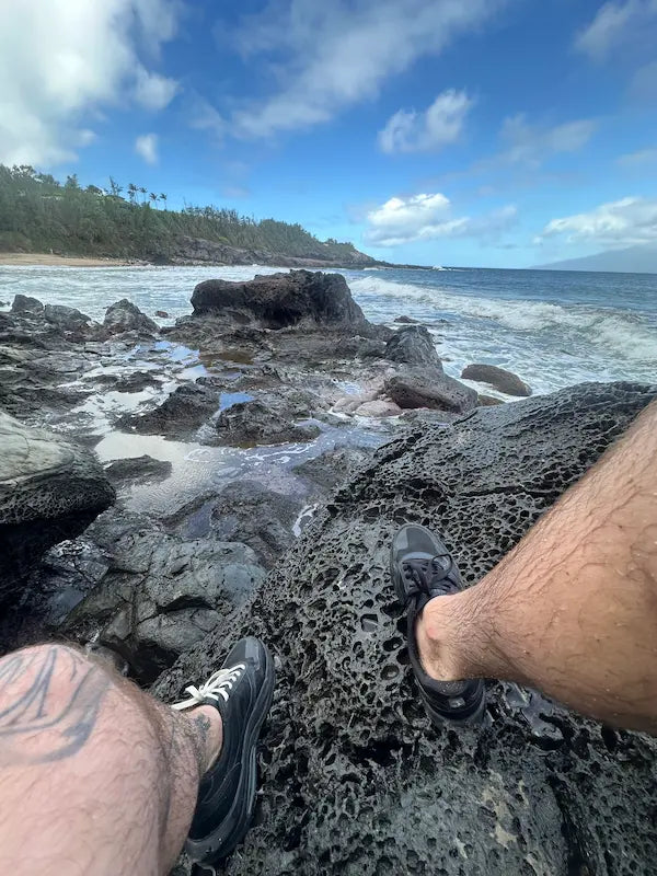 Person sitting on a rocky beach with ocean and sky in the background